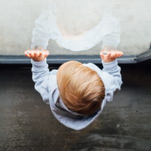 blonde haired boy in grey top leaning on glass door