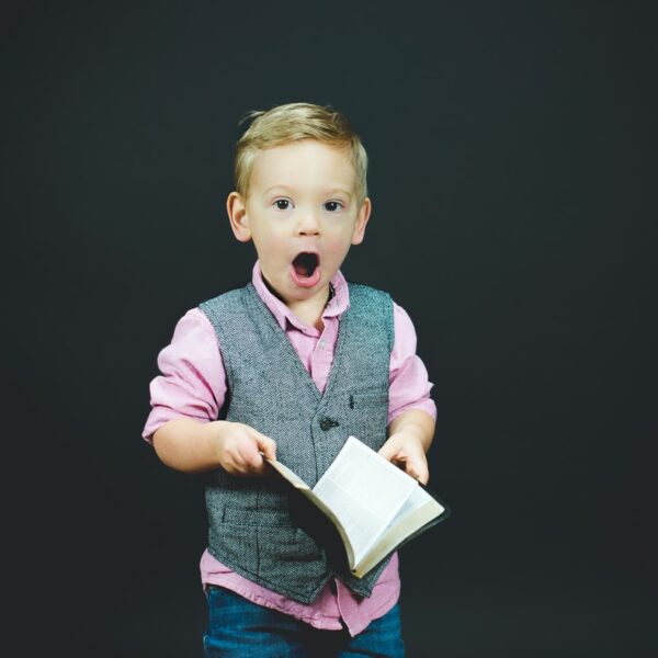 boy wearing gray vest and pink dress shirt holding book