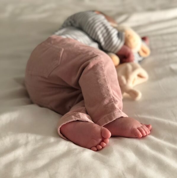 baby in gray and white striped long sleeve shirt and pink pants lying on white bed