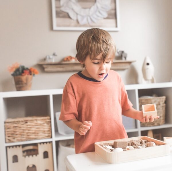 boy in orange crew neck t-shirt standing in front of white wooden table with cupcakes