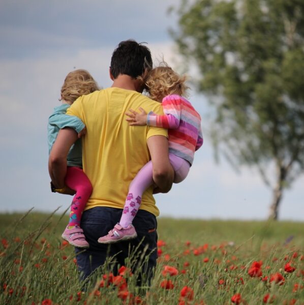 man carrying to girls on field of red petaled flower
