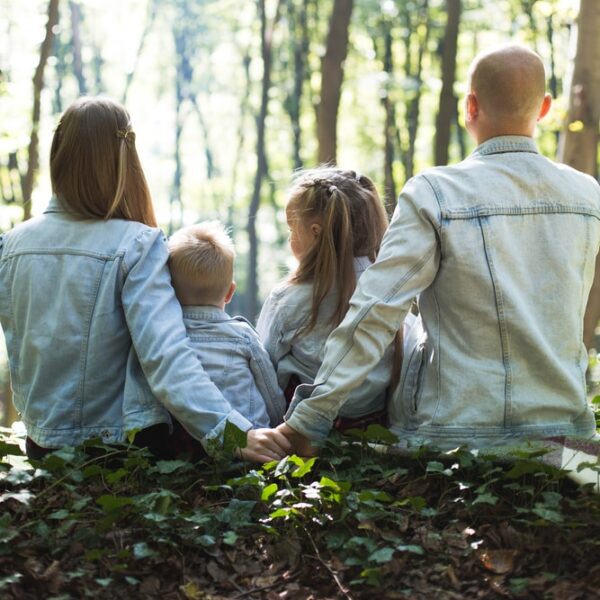 man and woman holding hands together with boy and girl looking at green trees during day
