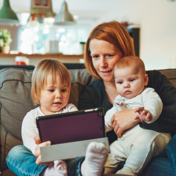 two babies and woman sitting on sofa while holding baby and watching on tablet
