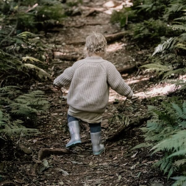boy in brown sweater and blue denim jeans walking on green grass during daytime