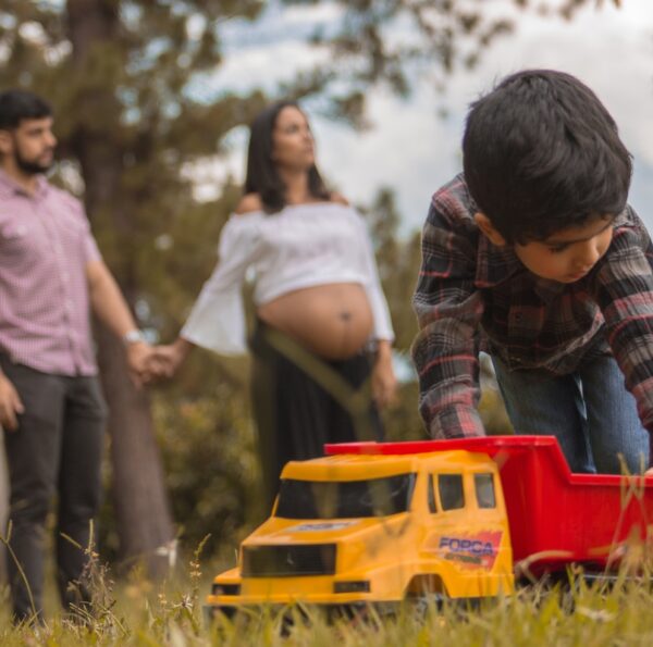 boy playing red and yellow truck on grass field
