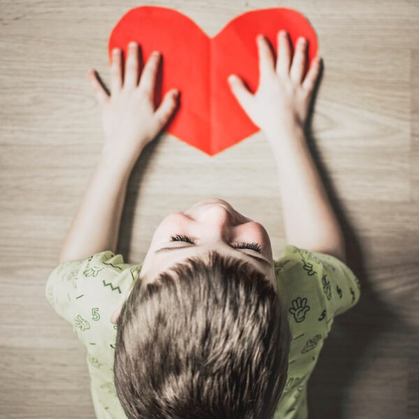 boy in green shirt holding red paper heart cutout on brown table