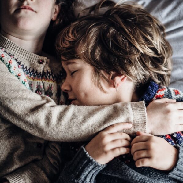girl and boy lying on bed wearing brown and grey sweatshirts