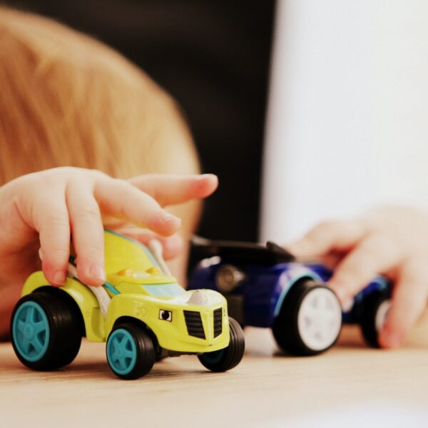 child playing with two assorted-color car plastic toys on brown wooden table
