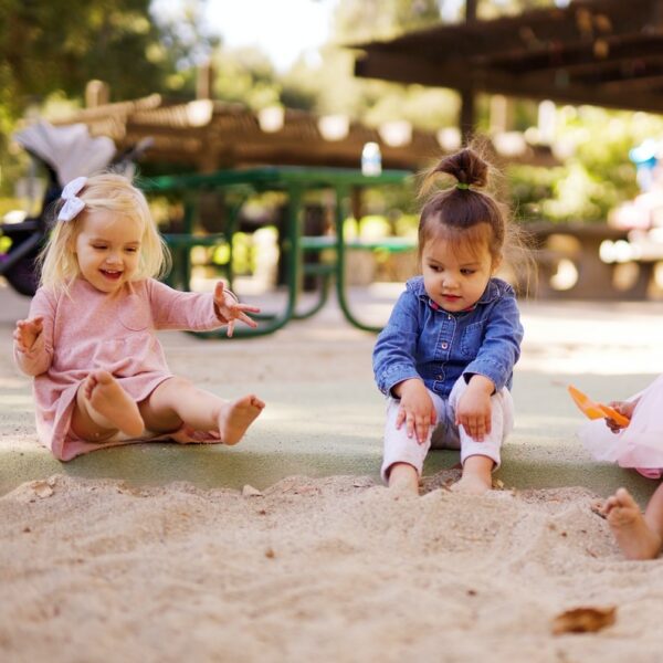 girl in pink dress sitting on brown sand during daytime
