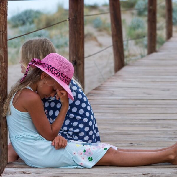 girl in blue and white polka dot shirt and pink hat sitting on wooden bridge