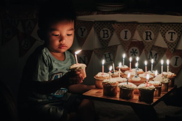 boy holding one of many cupcakes with lit candles