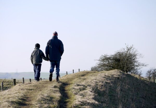 man and boy walking on grass near fence