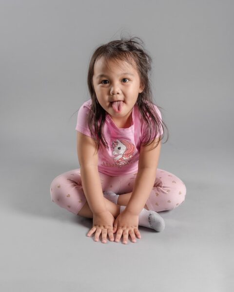 girl in pink shirt and pink pants sitting on pink and white polka dots ball